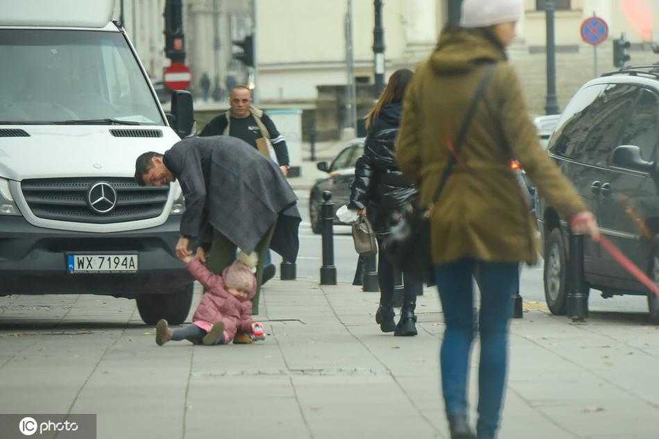 画面中莱万轻松地肩扛小女儿，一手轻扶着她，脸上带着灿烂而满足的笑容。安娜和大女儿克拉拉相伴左右，一家四口其乐融融，背景是充满生活感的城市街道，完美诠释了“铁汉柔情”的真谛。