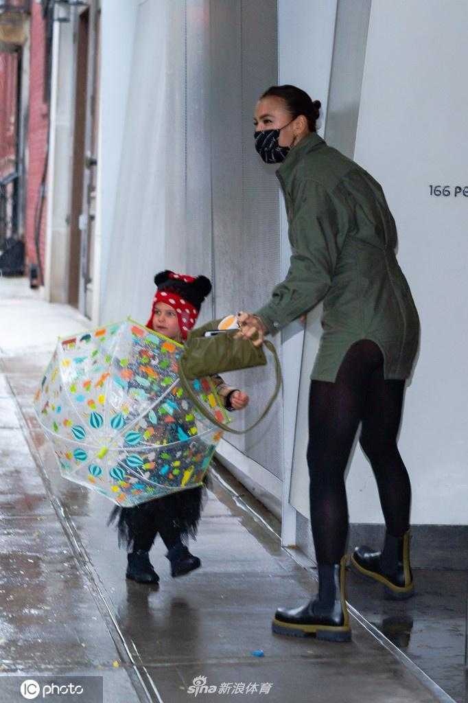 超模伊莉娜身穿深色休闲装，牵着女儿莉亚的小手走在纽约街头，她低头看向女儿，眼神中满是温柔与关爱，母女之间的互动温馨自然。