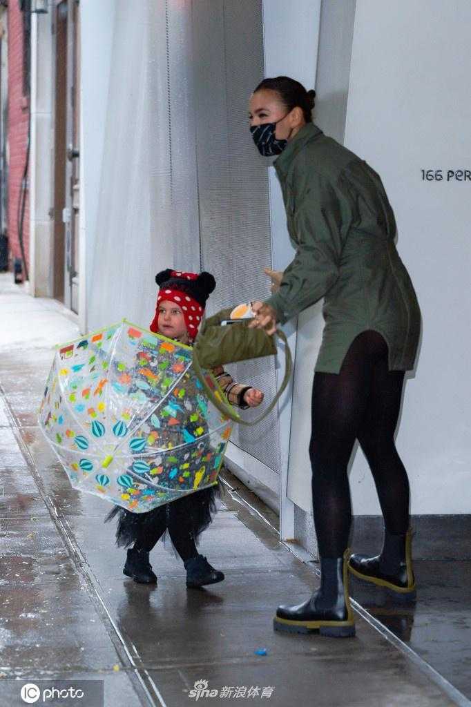 走在前面的莉亚，手拿小花伞回头张望，似乎在对妈妈说着什么。伊莉娜则面带微笑，耐心地倾听着女儿的话语，画面充满了母女间的亲密无间。