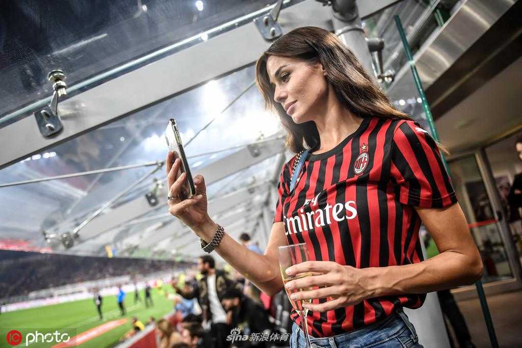 一位优雅的女士身着剪裁得体的黑色礼服，在圣西罗球场外回眸一笑，尽显意式风情与足球激情碰撞的魅力