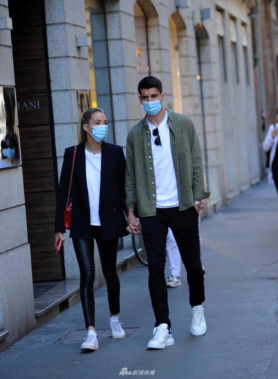 莫拉塔从背后轻轻环抱住爱丽丝，下巴轻抵在妻子的肩头，眼神中满是宠溺。爱丽丝则侧过脸，长发随风轻拂过莫拉塔的脸庞，两人在米兰的街角构筑起一个只属于他们的二人世界。