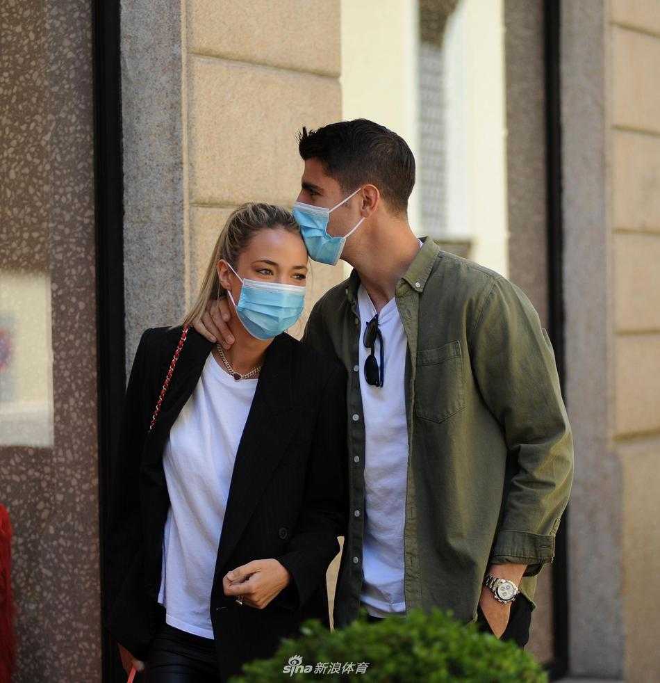 在商店橱窗前，莫拉塔耐心地陪伴爱丽丝挑选物品。莫拉塔双手插兜，面带微笑地看着妻子，眼神里没有丝毫的不耐烦，只有满满的欣赏与等待。