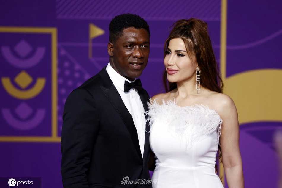 夫妇二人侧身低语，笑容灿烂，红毯灯光为他们的轮廓镀上金色光晕
