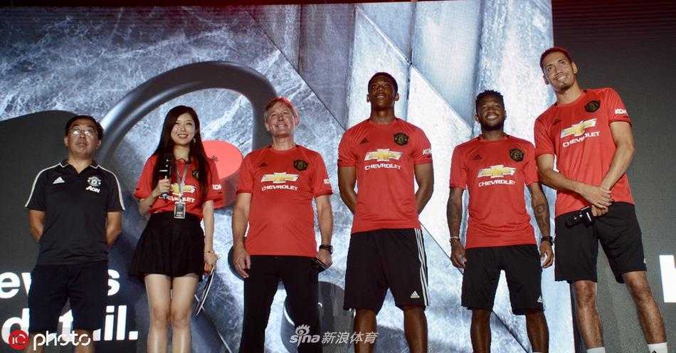活动现场座无虚席，身穿各式曼联球衣的球迷们全神贯注地注视着舞台，不时挥舞着手中的围巾和旗帜，汇成一片红色的海洋。