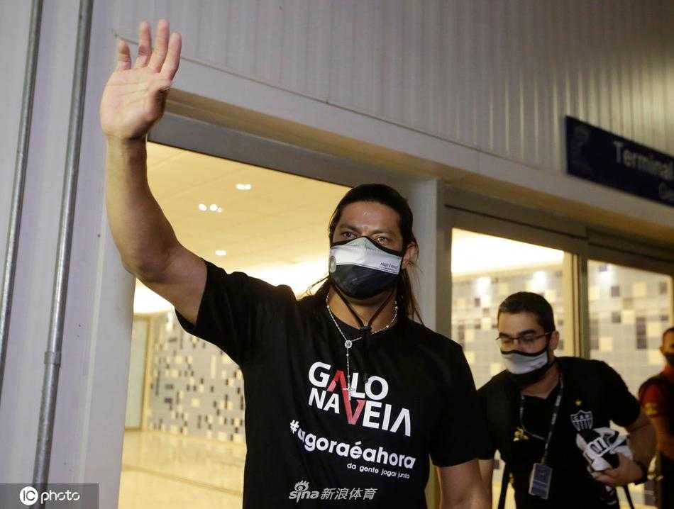 在机场通道中，胡尔克右手抱着一个可爱的玩偶，左手温柔地搭在妻子肩头。两人步伐一致，神情放松，背后是跟随的行李车，整个画面充满了家庭出行的温馨与对未来生活的憧憬。