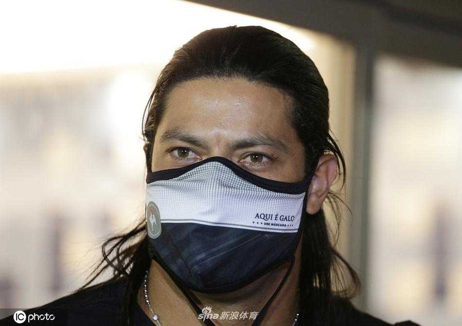 米内罗竞技俱乐部的吉祥物——一只威武的公鸡，张开双臂给了胡尔克一个大大的拥抱。胡尔克被这突如其来的热情逗得开怀大笑，现场气氛轻松而欢快，爱妻则在一旁用手机记录下这有趣的瞬间。
