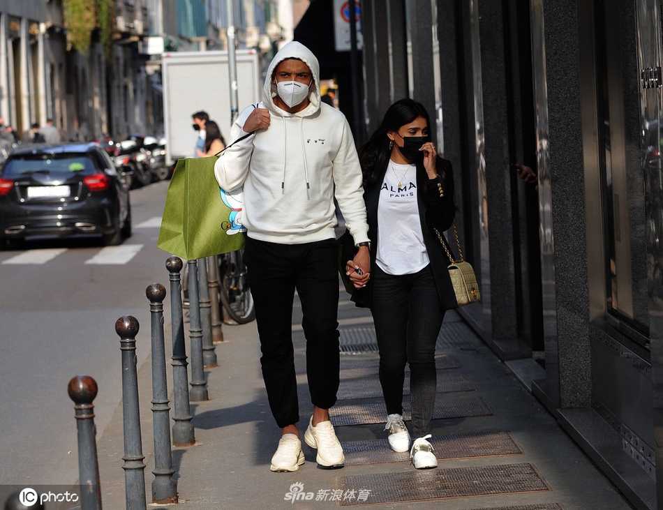 哥伦比亚射手穆列尔身着深色休闲装，与身穿米白色长款大衣的爱妻十指紧扣，两人步伐轻快地漫步在米兰奢侈品购物街，脸上洋溢着轻松惬意的笑容。