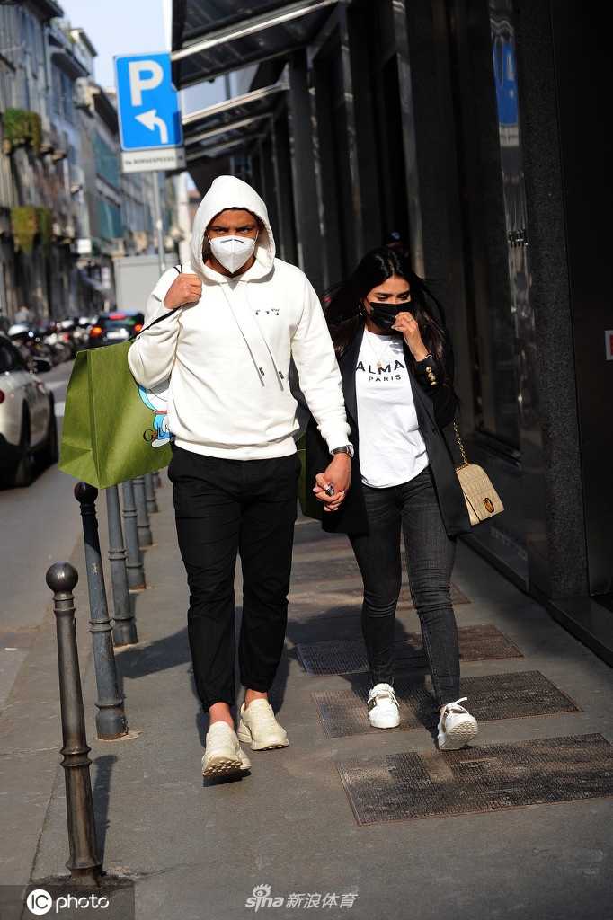 穆列尔的妻子身穿剪裁得体的浅色系大衣，手提疑似新购入的奢侈品纸袋，走在米兰标志性的拱廊街道上，穆列尔则像一名忠诚的卫士紧随其侧，画面充满了生活气息。