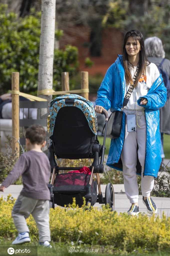 妻子萨拉推着婴儿车微笑注视前方，伊斯科侧身倾听家人交谈，家庭氛围宁静温馨