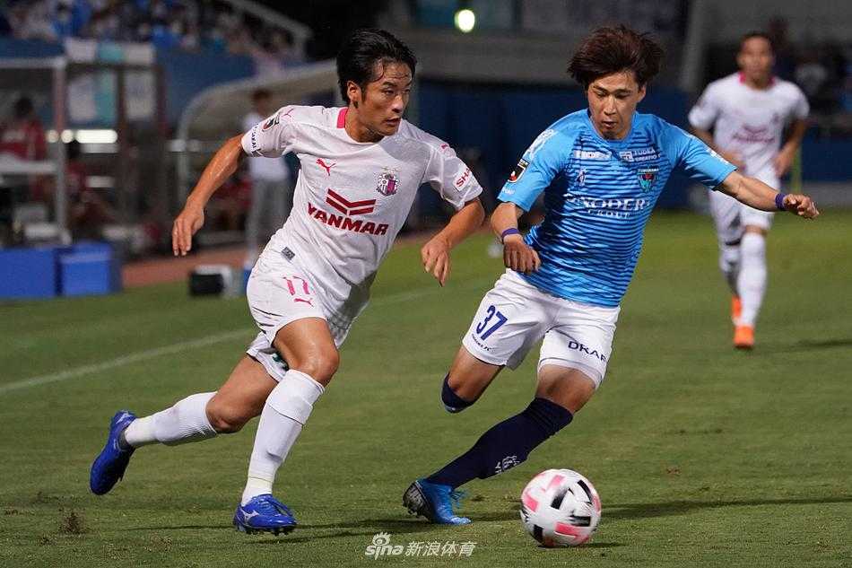 横滨FC后卫如临大敌，飞身铲抢试图截断大阪樱花核心球员的脚下球，草屑随着他的动作飞扬，整个画面充满了肌肉碰撞的力量感