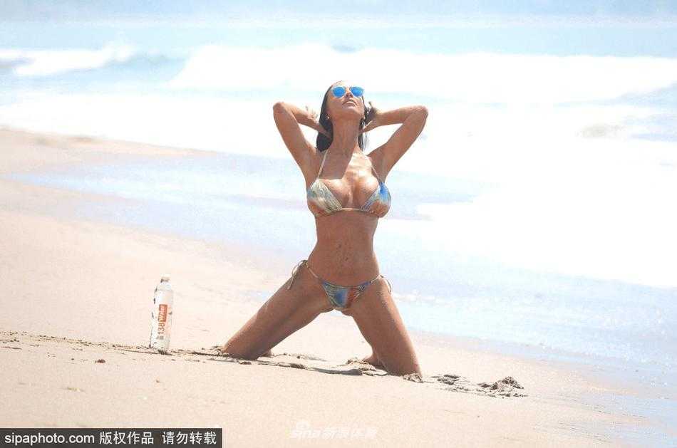 查理·里娜背对夕阳站立，回眸瞬间长发飞舞，金色光线勾勒出完美的身体轮廓，画面极具张力