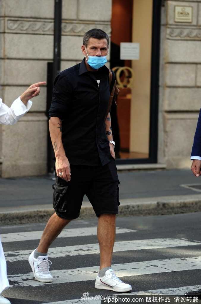 博班身穿簡潔的白色Polo衫，搭配休閒長褲，與身穿淺色連衣裙的妻子米蘭達並肩走在米蘭街頭。他神情放鬆，正側耳傾聽妻子說話，眼神中充滿了溫柔與專注，仿佛此刻的世界只有他們二人。