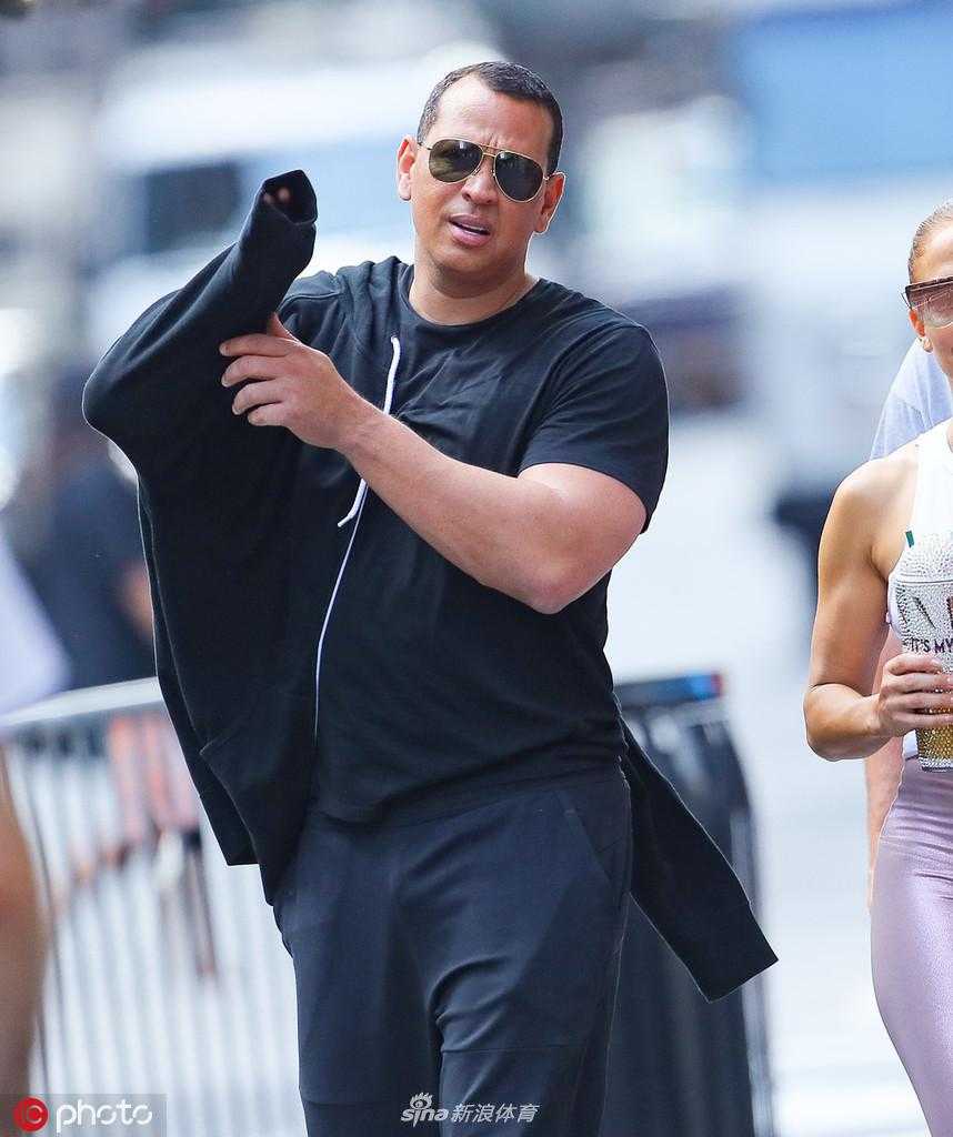 洛佩兹侧身微笑，紧身裤的修身效果将她的身材曲线衬托得凹凸有致，手中的饮品仿佛是对刚刚努力训练的甜蜜奖励。