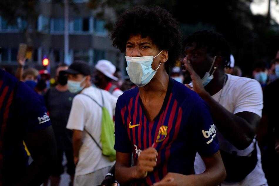 在一群情緒激動的成年球迷之中，一位戴著巴薩帽子的小男孩靜靜地站在護欄邊，他稚嫩的臉上寫滿了與年齡不符的憂傷，小手緊緊抓著護欄，眼神透過人群望向遠方，彷彿在等待一個永遠不會出現的奇蹟。