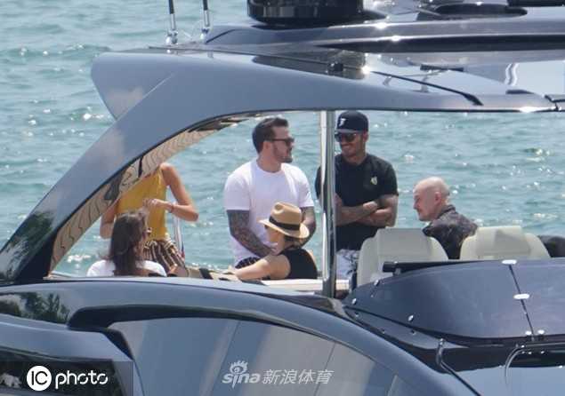贝克汉姆与次子罗密欧在游艇甲板上亲密并肩，父子二人笑容灿烂。罗密欧身穿蓝色休闲上衣，尽显年轻人的活力，背景是湛蓝的天空与大海