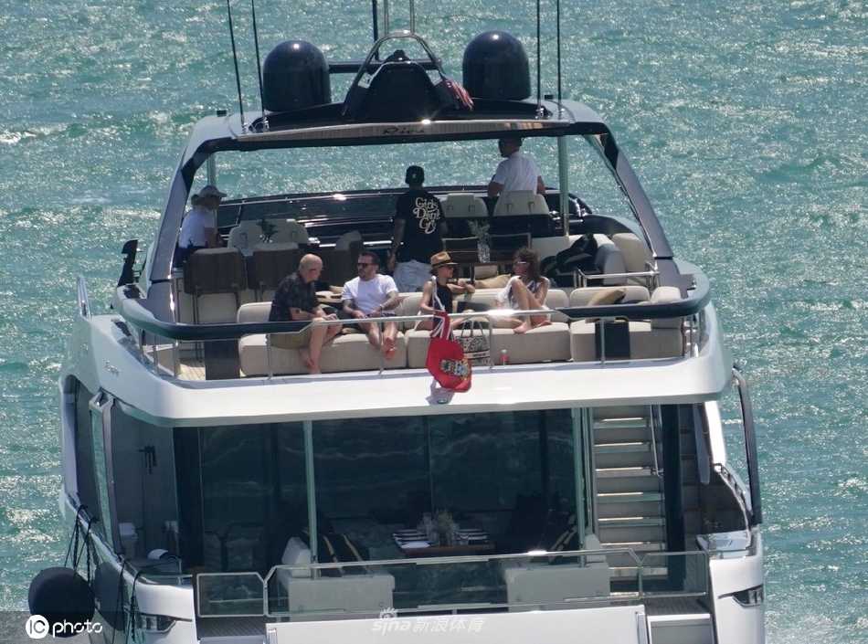 游艇的侧后方全景，洁白的船体线条优雅，在湛蓝海水的映衬下格外醒目。可以清晰看到尾部的游泳平台，以及船舱宽敞明亮的窗户，尽显豪华游艇的现代感与设计感