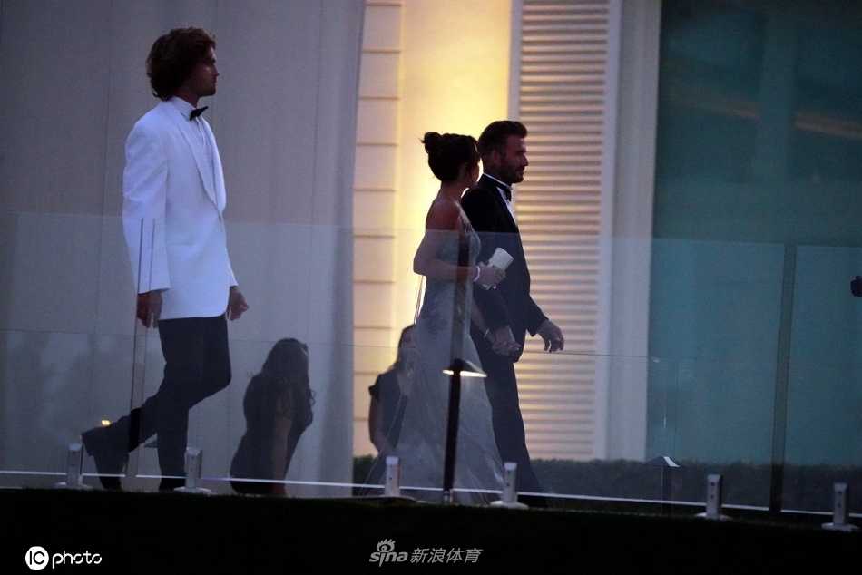 贝克汉姆夫妇并肩漫步于婚礼草坪，大卫的手轻轻搭在维多利亚腰间，两人步调一致，眼神中流露出历经岁月沉淀的默契与温情。