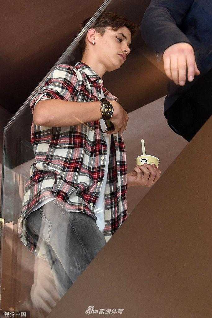父子俩在米兰古老街道上驻足，小贝低头看向儿子，似乎在叮嘱什么，儿子认真聆听，画面充满温情。