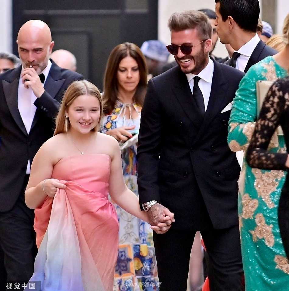 贝克汉姆紧牵女儿小七走上红毯，父亲身着深色西装帅气挺拔，女儿仰头甜笑，画面温馨有爱