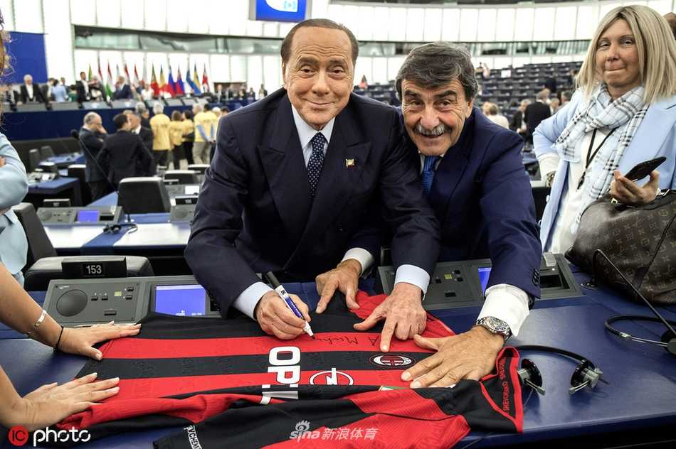 贝卢斯科尼与两位政要友人共同举起AC米兰红黑间条衫，身后是欧盟会议走廊，三人都露出会心笑容，轻松一刻被镜头捕捉。