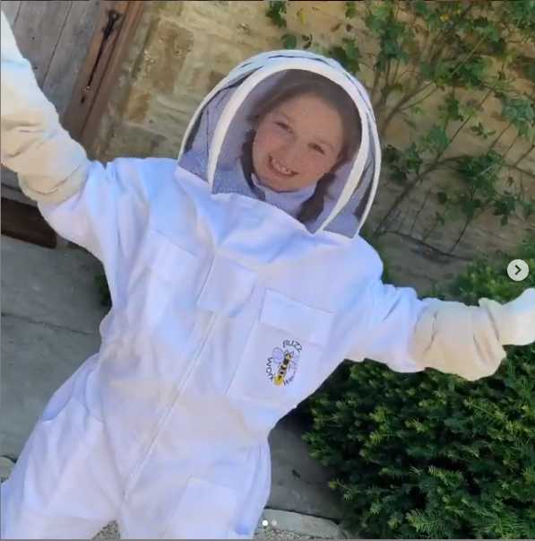 小七身穿素雅碎花裙，一头柔软的金色长发被精心编成温婉的辫子，她微微侧身，对着镜头露出恬静而羞涩的微笑，宛如油画中走出的田园小天使。