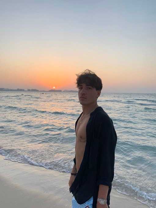他侧身回眸，身后是碧蓝的海水与天空，阳光为他勾勒出金色的轮廓，湿漉漉的发梢滴落水珠，充满电影质感的瞬间